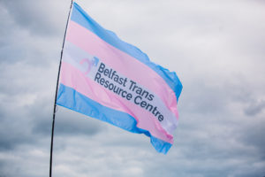 A large trans flag emblazoned with the Belfast Trans Resource Centre logo, free flying on a pole